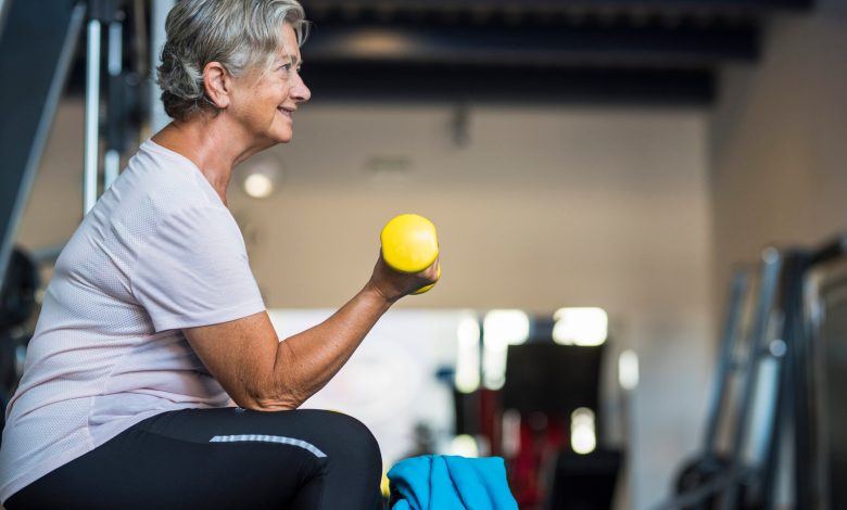 mature woman at the gym training her body and her biceps sitting in a bench with a dumbbell in her hand - healthy and fitness senior lifestyle