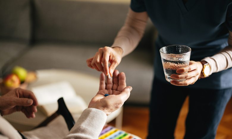 Anonymous female nurse giving pills and water to an unrecognizable senior man at the nursing home.