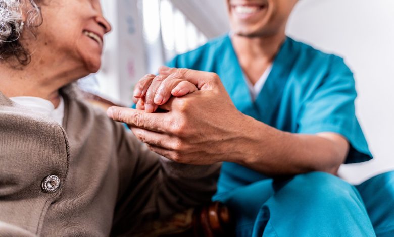 Senior woman holding caregiver's hands at home