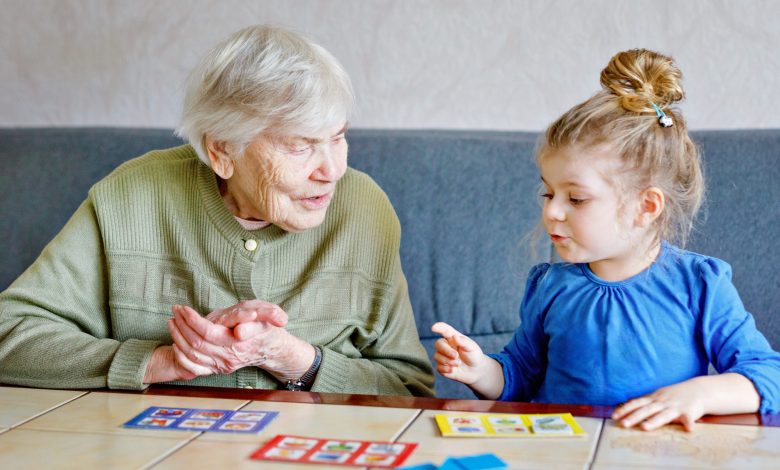 Beautiful toddler girl and grand grandmother playing together pictures lotto table cards game at home. Cute child and senior woman having fun together. Happy family indoors.