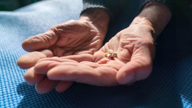 Senior hands with various pills resting on a blue mat, illuminated by warm natural sunlight