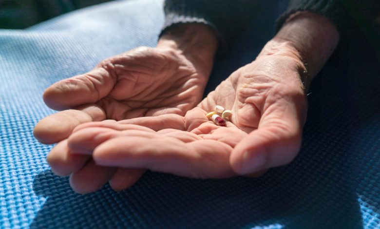 Senior hands with various pills resting on a blue mat, illuminated by warm natural sunlight