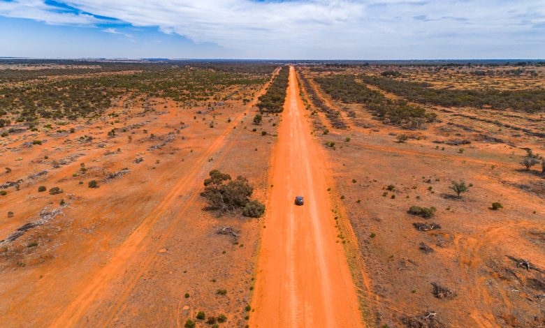 Straight red orange dirt road in outback Australia with single car driving
