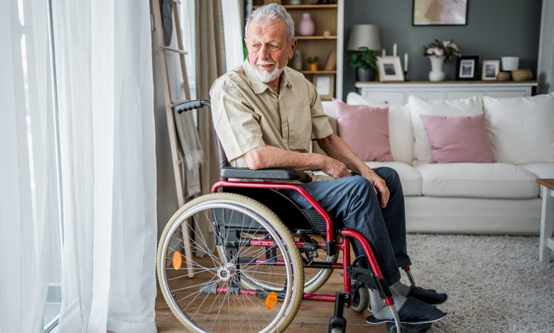 Pensive senior man in a wheelchair looking through the window at his home