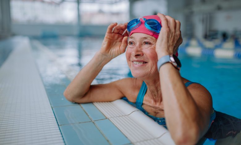 A happy senior woman in swimming pool, leaning on edge.
