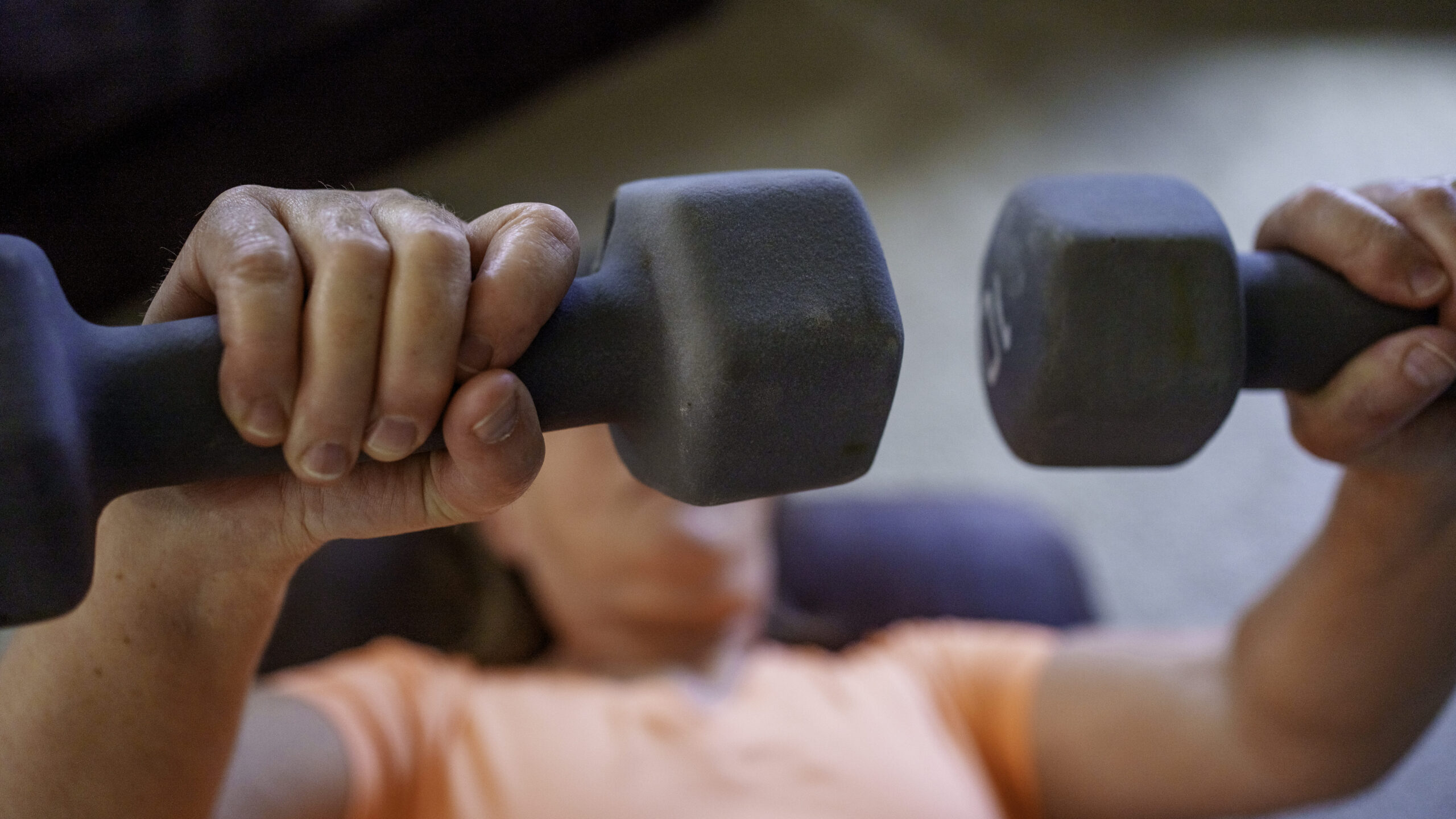 Downward Looking Clip Woman in Her Sixties Working Out at Home with Dumbbells Doing Bench Presses on an Ottoman in Her Living Room