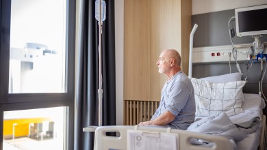 In a hospital setting, an elderly man sits up in his bed, looking out the window. The room is well-equipped with medical devices and provides a sense of comfort during his recovery.