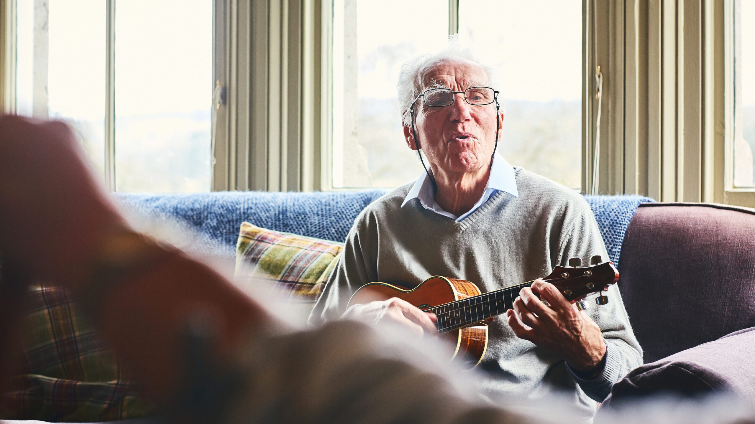 Happy senior man singing song and playing guitar for a woman sitting in front at home