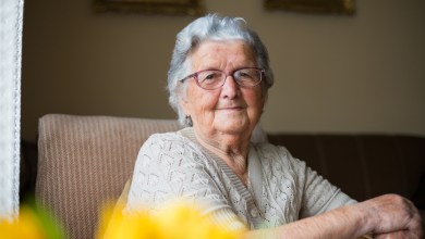Portrait of a beautiful old woman with gray hair and glasses is sitting in a chair in her home.