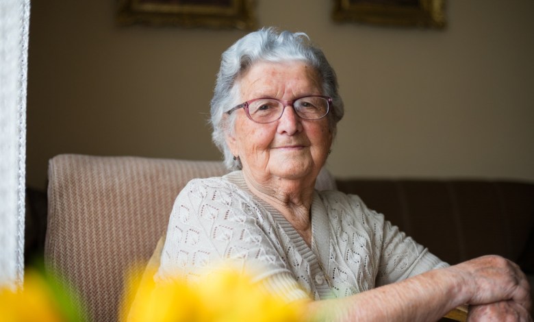 Portrait of a beautiful old woman with gray hair and glasses is sitting in a chair in her home.